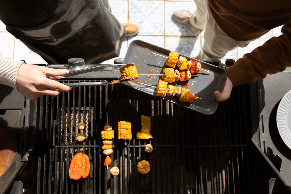 A father and son grilling vegetables together in their custom outdoor kitchen and bar in Leawood. One of them is holding tongs with corn, and the other has a platter with some skewers of grilled vegetables.